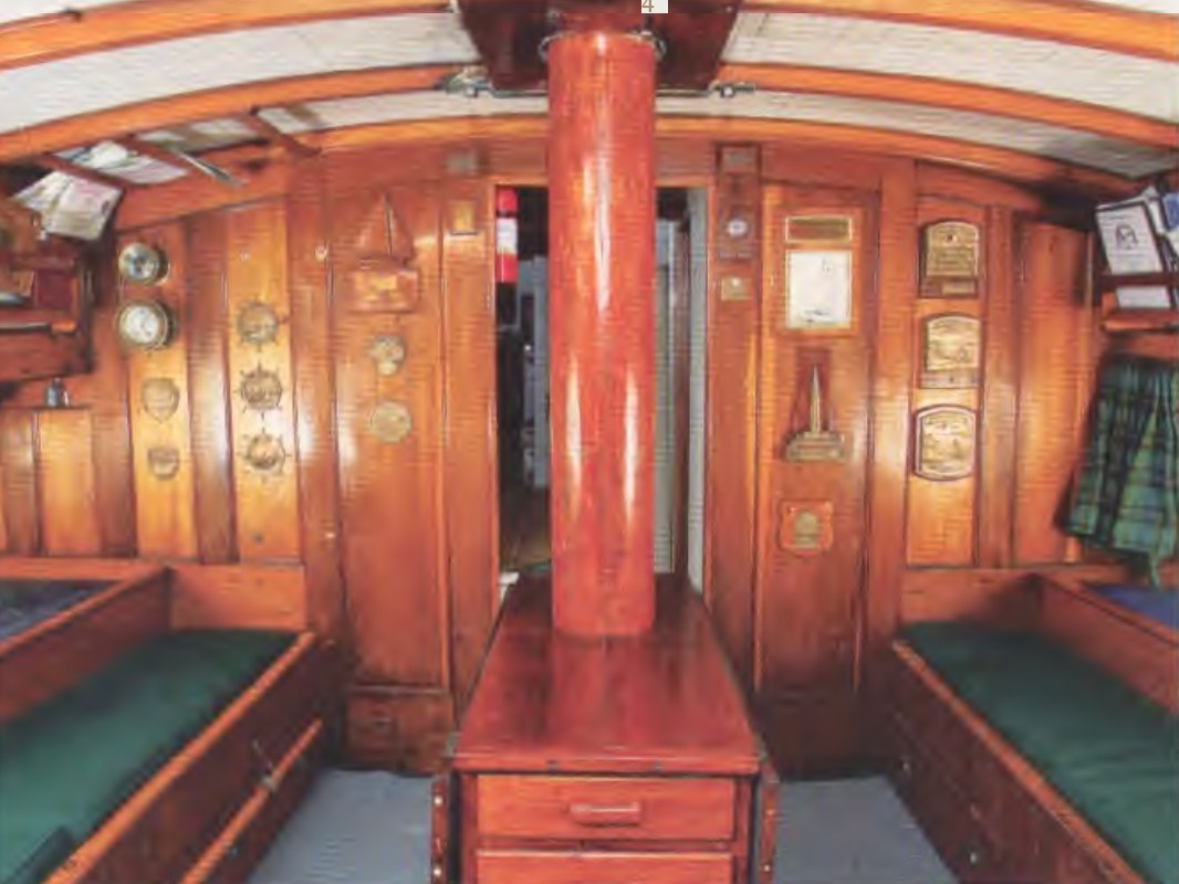 Yankee's main saloon: banquette seating both sides, trophy plaques on the bulkheads, the mainmast through the cabin