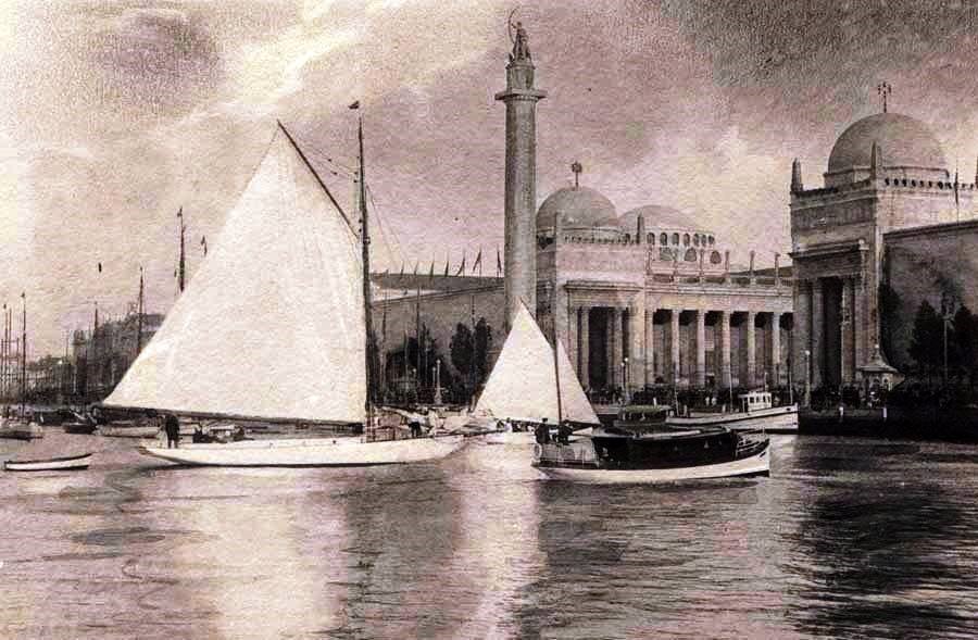 A gaff sloop believed to be Yankee sailing past the pavilions of the 1915 Panama Pacific International Exposition